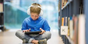 child with headphones reading a tablet