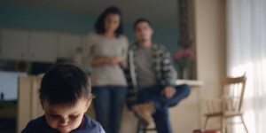 young child looking sad with parents blurred out in background