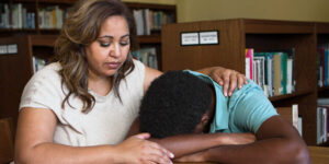 kid with head in his arms and adult patting his back