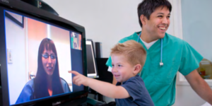 doctor with child pointing at monitor screen that displays a therapist