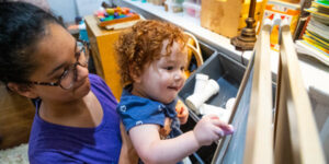 preK teacher holding up young child to paint